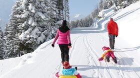Familie beim Schlittenfahren in verschneiter Winterlandschaft. © Sport Kessler GmbH
